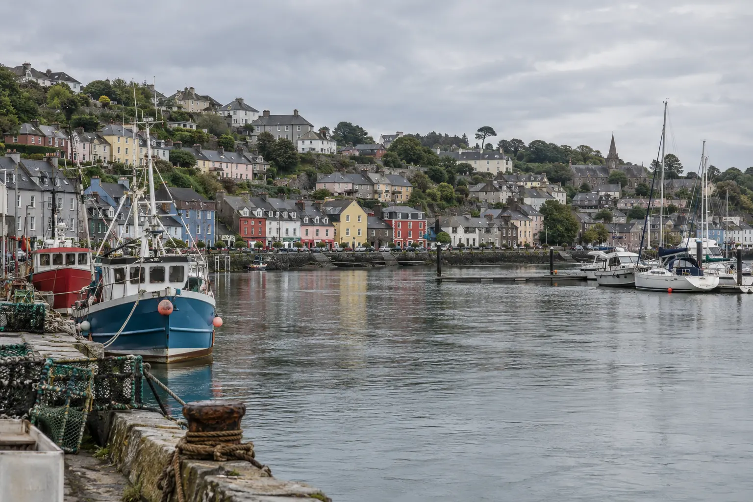 A harbour town with moored boats and terraced houses under an overcast sky